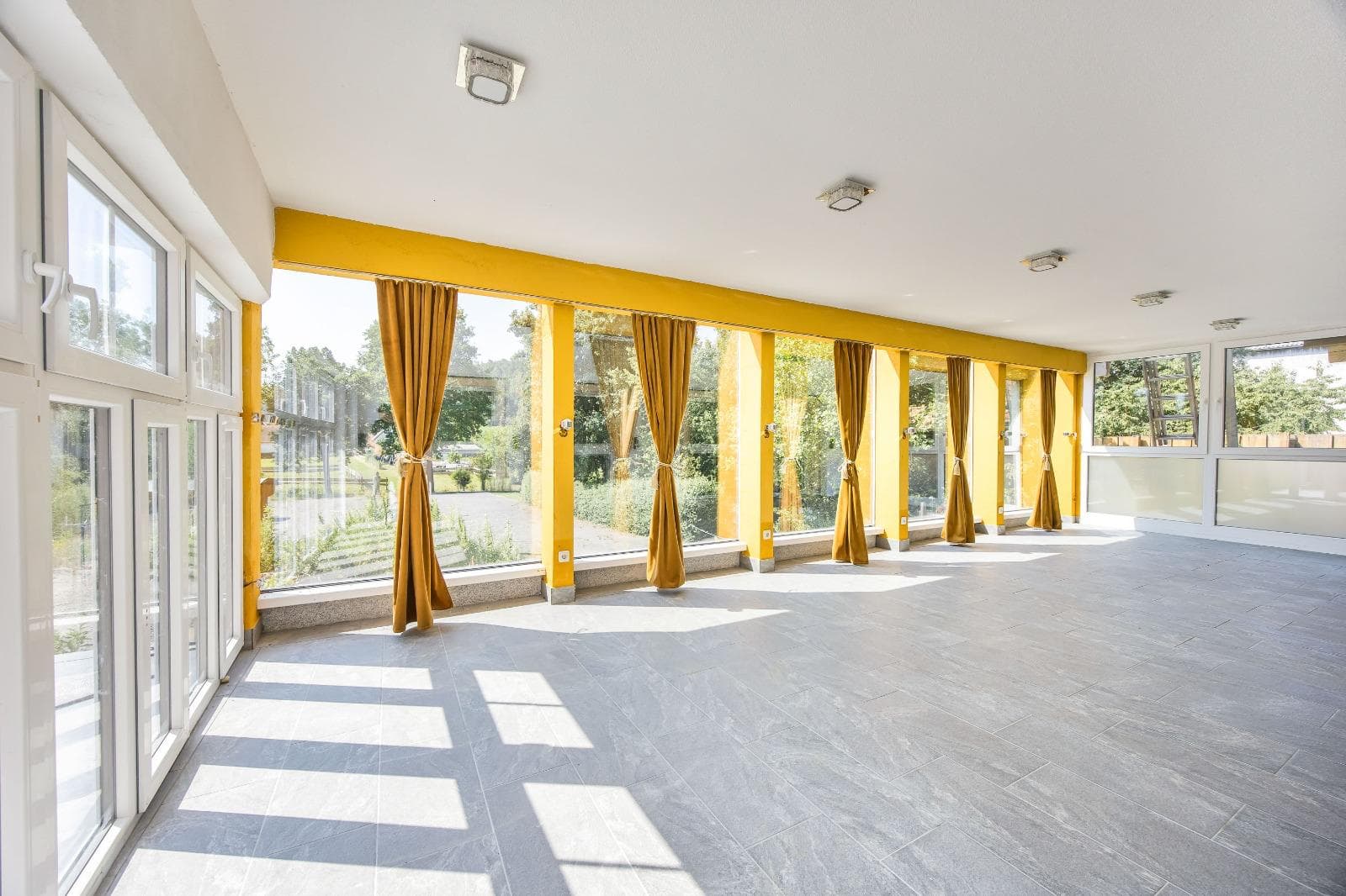Lichtdurchfluteter Saal mit goldenen Vorhängen und heller Diele